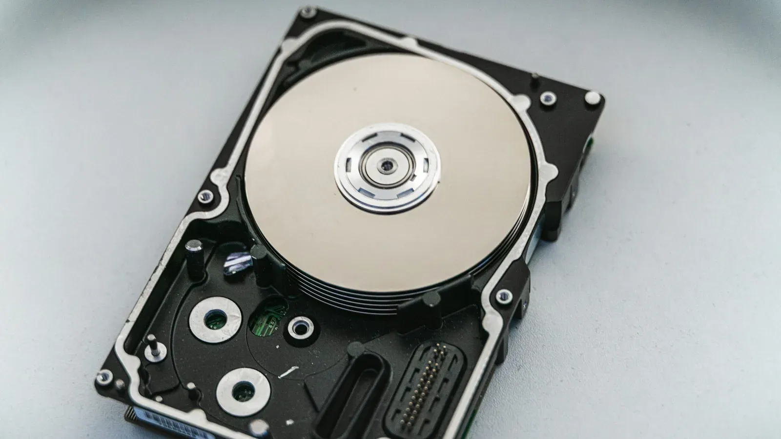 Un hard disk deschis, cu discul magnetic și brațul de citire vizibile, pe o suprafață albă